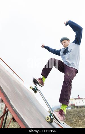 Teenager Skater in Hoodie Sweatshirt und Jeans gleiten über ein Geländer auf einem Skateboard in einem Skatepark, Weitwinkel Stockfoto