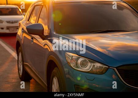 Luxuriöser SUV mit modernem Design, parkt bei Sonnenuntergang am Straßenrand. Vorderansicht des blauen Fahrzeugs als Symbol für Geschäftserfolg und umweltfreundliche Technologie. Stockfoto