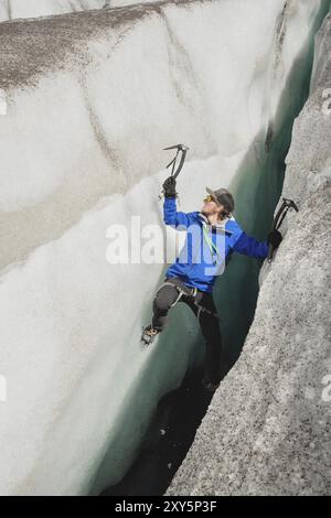 Ein freier Kletterer ohne Versicherung mit zwei Eisachsen steigt aus einem Riss im Gletscher auf. Freies Klettern ohne Seile Stockfoto