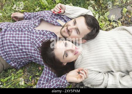 Ein liebevolles Paar Hipster liegt in einer Umarmung auf dem Gras und streichelt sich gegenseitig Stockfoto