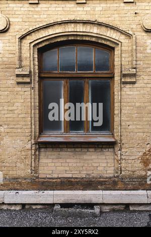 Vintage Bogenfenster in der Wand aus gelbem Ziegelstein. Schwarzes Glas in einem dunkelroten Holzrahmen. Das Konzept der antiken Vintage-Architektur im Bau Stockfoto