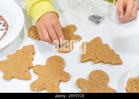 Kinderhände, die Weihnachtskekse schmücken. Kind, das Lebkuchenkekse dekoriert Stockfoto