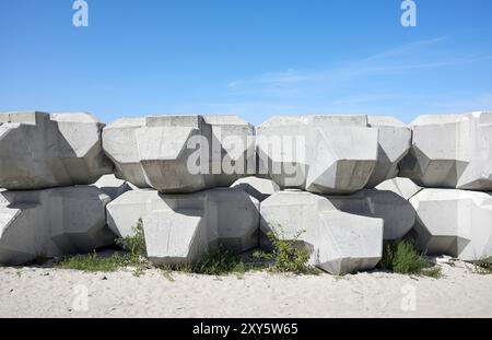 Wellen, die Betonblöcke am Strand ableiten. Stockfoto