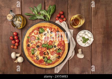 Overhead Foto von Pepperoni Pizza mit Glas Weißwein, Olivenöl, Basilikum, Champignons, Tomaten und Käse mozzarellini, geschossen von Abo Stockfoto