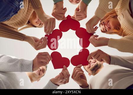 Unteransicht einer fröhlich lächelnden Gruppe von Menschen, die rote Herzen in den Händen halten. Stockfoto