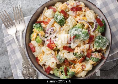 Salat mit Blumenkohl, Brokkoli, gekochtem Speck, Käse und roten Zwiebeln auf der Schüssel auf dem Tisch. Horizontale Draufsicht von oben Stockfoto