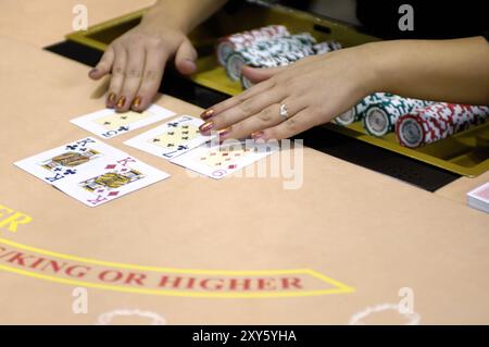 Hände eines weiblichen Croupiers an einem Blackjack-Kartentisch, der die Karten in einem Casino ausgibt Stockfoto