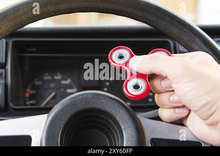 Nahaufnahme eines Mannes, der mit einem Spinner spielt, während er in einem Stau sitzt, auf dem Hintergrund des Lenkrads eines beliebten Fidget-Spinner-Spielzeugs im Auto Stockfoto