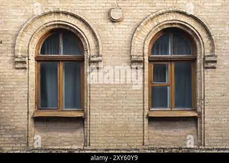 Zwei alte Bogenfenster in einer Wand aus gelben Ziegeln. Grün, die Farben von Meereswellen-Glas in einem braunen dunkelroten Holzrahmen. Das Konzept des antiken V Stockfoto