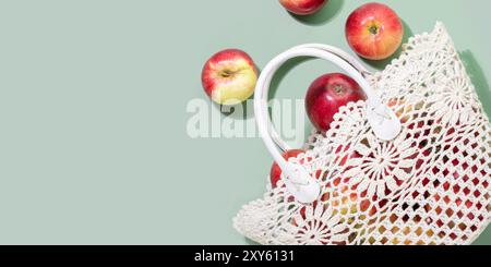 Rote Äpfel, die aus der gehäkelten Tasche auf pastellgrünem Hintergrund verschüttet werden Stockfoto