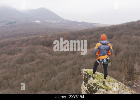 Hipster, ein Kletterer in einer Daunenjacke und einer Strickmütze steht und meditiert, während er auf das herbstliche Ponamramu des benachbarten Moun blickt Stockfoto