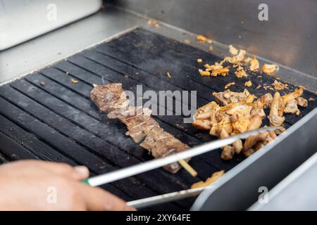 Eine Person kocht Antikuchos auf einem Grill. Das Fleisch wird auf Spießen gekocht und wird von anderem Fleisch umgeben Stockfoto