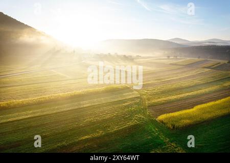 Spektakuläres Sonnenaufgangslicht über den nebeligen Maisfeldern in der Nähe einer kleinen Dorfgemeinde in der Nähe von Dolenjske toplice in der Region Dolenjska, Slowenien Stockfoto