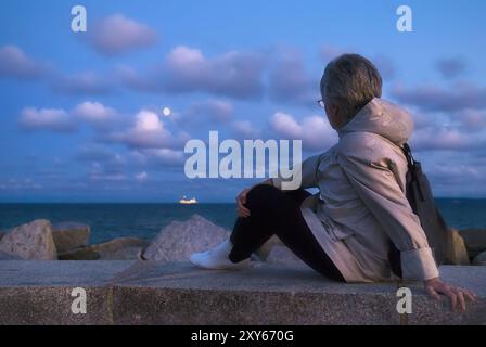 Frau sitzt auf dem Pier und blickt aufs Meer Stockfoto