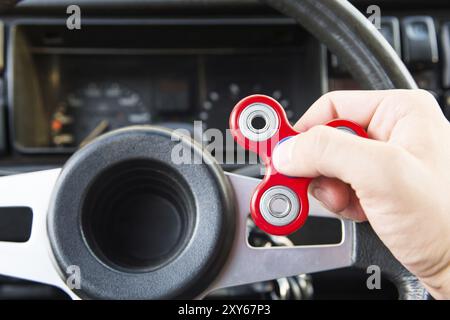 Nahaufnahme eines Mannes, der mit einem Spinner spielt, während er in einem Stau sitzt, auf dem Hintergrund des Lenkrads eines beliebten Fidget-Spinner-Spielzeugs im Auto Stockfoto