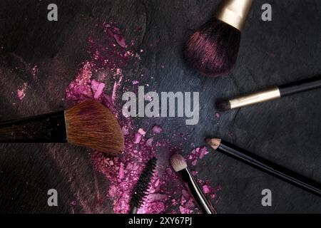 Make-up-Pinsel mit zerquetschten Kosmetik, geschossen von oben auf einem schwarzen Hintergrund bilden einen Rahmen für Kopie, eine Schönheit design Vorlage für eine Make-up-ba Stockfoto