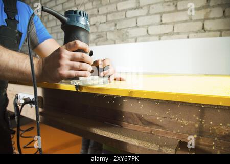 Der professionelle Zimmermann verarbeitet die Kunststoffkanten der Arbeitsplatte mit einem speziellen Elektrowerkzeug Stockfoto