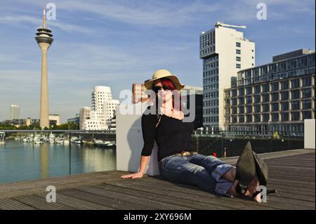 Eine junge Frau mit Strohhut sitzt im Düsseldorfer Medienhafen Stockfoto