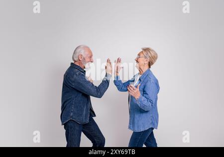 Seitenansicht eines aufgeregten Seniorenpaares, das High-Five gibt und Erfolg auf weißem Hintergrund feiert Stockfoto