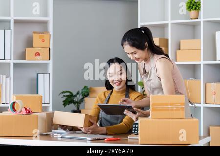 Zwei Unternehmerinnen, die in einem kleinen Büro arbeiten, umgeben von Versandkartons und mit einem digitalen Tablet Stockfoto