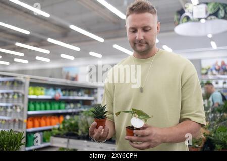 Porträt eines lächelnden jungen bärtigen Mannes in grünem T-Shirt, der während der Pflanzensammlung im Geschäft für Haushaltswaren hält. Pflanze, Natur, Einkaufskonzept Stockfoto