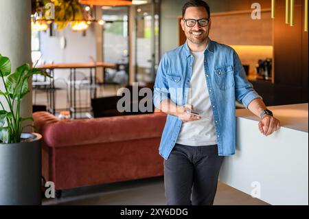Porträt eines selbstbewussten männlichen Ingenieurs, der im Büro lächelt und über das Smartphone SMS schreibt Stockfoto