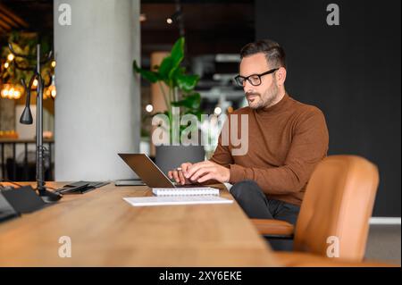 Fokussierter männlicher Programmierer in Brillen arbeitet ernsthaft an Projekten über Computer am Schreibtisch im Büro Stockfoto