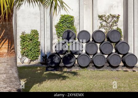 Gestapelte Sherry-Fässer auf Paletten vor einer Betonwand mit grünen Pflanzen und einer Palme im Sonnenlicht, Jerez de la Frontera, Andalusien, Spanien, Stockfoto