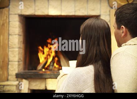 Paar Tassen mit heiße Schokolade mit Marshmallows vor brennenden Kamin hält Stockfoto
