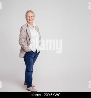 Lächelnde Geschäftsfrau mit Händen in den Taschen, die selbstbewusst auf isoliertem weißen Hintergrund posiert Stockfoto