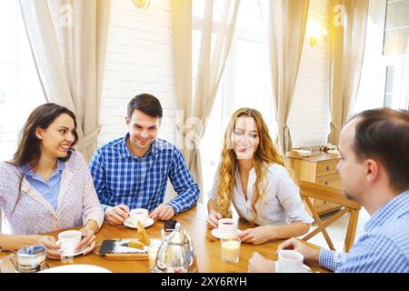 Gruppe von vier glückliche Freunde treffen und reden und Essen von Nachtischen auf einem Tisch zu Hause Stockfoto