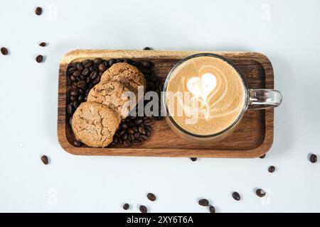 Tasse Kaffee mit Herzform im Schaum mit Kaffeebohnen und Keks auf weißem Hintergrund Stockfoto