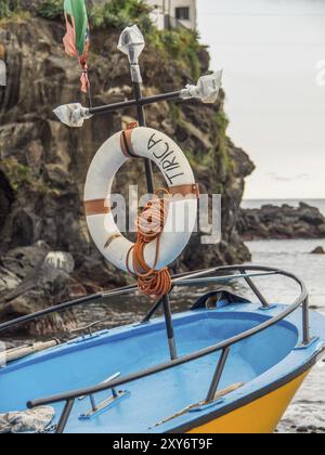 Kleines Boot mit Rettungsschirm und Seil am Ufer neben Felsen, Funchal, madeira, portugal Stockfoto