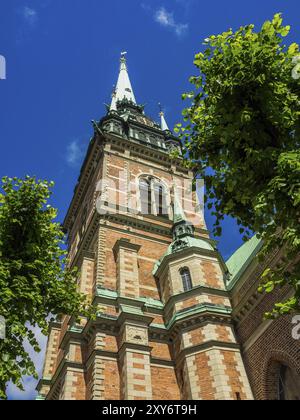 Imposanter gotischer Kirchturm mit Backsteinmauern, umgeben von Bäumen vor blauem Himmel, stockholm, ostsee, schweden, skandinavien Stockfoto