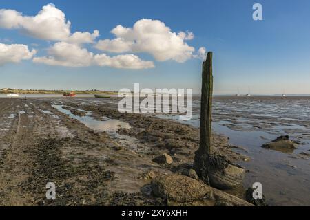 Ein hölzerner Pfosten mit einigen Wolken, gesehen in den Oare Marshes in der Nähe von Faversham, Kent, England, Großbritannien, mit einigen Booten und der Isle of Sheppey im Hintergrund Stockfoto