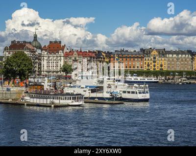 Verschiedene Boote und Schiffe im Hafen vor einer Reihe von bunten Stadtgebäuden unter blauem Himmel, stockholm, ostsee, schweden, skandinavien Stockfoto