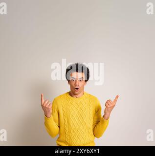 Ängstlicher junger Verkäufer, der auf den Kopierraum zeigt und schockiert auf die Kamera auf weißem Hintergrund blickt Stockfoto