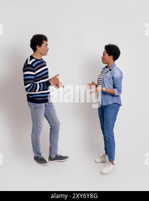 Seitenansicht eines jungen Paares, das sich ansieht und darüber spricht, während er über weißem Hintergrund steht Stockfoto