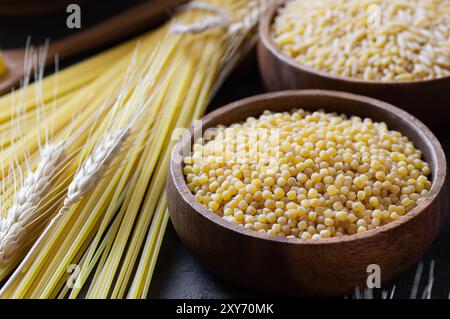 Rohe Couscous in Schüssel auf hölzernem Hintergrund mit Weizen, ungekochtes Essen Konzept Stockfoto