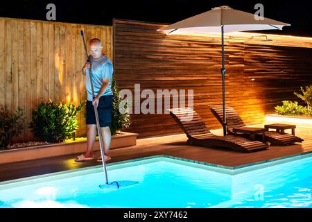 Mann, der den Swimmingpool mit einem Netz reinigt, entfernt Blätter und Wanzen Stockfoto