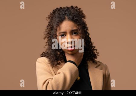 Afrikanisches Teenager-Mädchen hat Schmerzen. Frau mit geschwollener Kehle im beigefarbenen Studio. Angina Pectoris Stockfoto