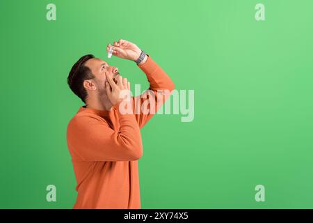 Seitenansicht eines jungen Mannes mit Bindehautentzündung, der Tropfen zur Behandlung auf isoliertem grünen Hintergrund setzt Stockfoto