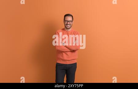 Porträt eines entschlossenen jungen Geschäftsmannes mit überkreuzten Armen, der selbstbewusst auf orangefarbenem Hintergrund posiert Stockfoto