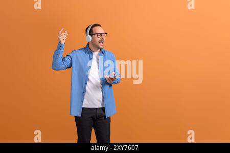 Junger Mann mit geschlossenen Augen, Gesang und Musik über Kopfhörer auf orangefarbenem Hintergrund Stockfoto