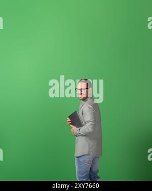 Seitenansicht eines erfolgreichen Geschäftsmannes mit Laptop, der die Kamera über die Schulter auf grünem Hintergrund lächelt Stockfoto