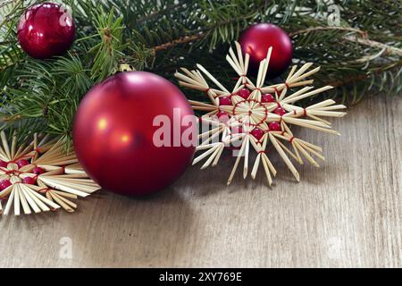 Weihnachten- und Neujahrsdekoration mit roten Kugeln und Strohsternen auf Holz, wenig Kopierraum für Grüße Stockfoto