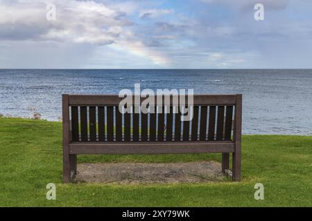 Eine Bank mit einem Regenbogen über der Nordsee Küste, im Benthall, Northumberland, England, UK gesehen Stockfoto