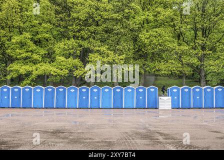 Lange Reihe tragbarer Toiletten vor einem Wald, wo man umkippt Stockfoto