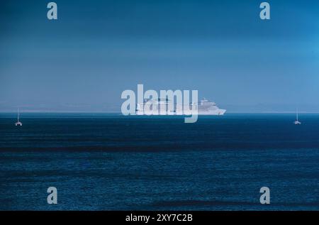 Ein großes Kreuzfahrtschiff gleitet durch das ruhige Meer mit einem klaren blauen Himmel und schafft an einem sonnigen Tag eine ruhige Atmosphäre Stockfoto