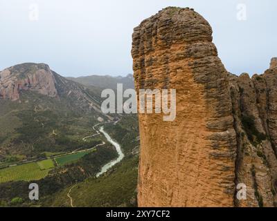 Blick auf einen riesigen Felsen, ein Tal mit einem Fluss und einer beeindruckenden natürlichen Kulisse, aus der Vogelperspektive, Las Penas de Riglos, wie Penyas de Riglos, Mallos de Stockfoto